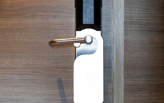 Paper black blank door hanger on wooden door with metal silver handle. Door hanger mockup. Design template.