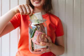 Girl removing five euro banknote from glass jar