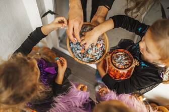 Children happy to receive many sweets and gifts. All girls wearing in bright witch of fairy dresses. Happy childhood. American traditional culture of Halloween celebration. Top view, copy space background with unrecognizable people.