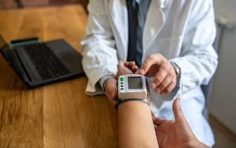 An old female patient is sitting at the doctor's office during a medical exam. A young doctor is measuring the blood pressure of a senior patient. The patient is sitting still while the doctor is examing her.