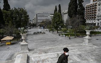 TOPSHOT - A man wearing a protective face mask walks at empty Athens' empty Syntagma square on March 23, 2020 as the country struggles to control the spread of the COVID-19, the novel coronavirus. (Photo by Aris Messinis / AFP) (Photo by ARIS MESSINIS/AFP via Getty Images)