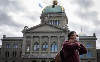 A tourist wearing a mask is seen in front of the Swiss House of Parliament on March 13, 2020, in Bern ahead of the announcement by Swiss government of new preventive measures against the spread of the COVID-19 caused by the novel coronavirus. (Photo by Fabrice COFFRINI / AFP) (Photo by FABRICE COFFRINI/AFP via Getty Images)