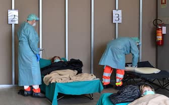 Hospital employees wearing protection mask and gear tend to patients lying in bed at a temporary emergency structure set up outside the accident and emergency department, where any new arrivals presenting suspect new coronavirus symptoms will be tested, at the Brescia hospital, Lombardy, on March 13, 2020. (Photo by Miguel MEDINA / AFP) (Photo by MIGUEL MEDINA/AFP via Getty Images)