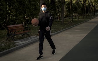 WUHAN, CHINA - APRIL 13: A man wearing a mask and gloves walks with a basketball in Jiangtan park on April 13, 2020 in Wuhan, Hubei Province, China. Despite the partial lift of the 76 day long lockdown, Wuhan's residential communities are still strictly controlling the flow of people. (Photo by Getty Images)