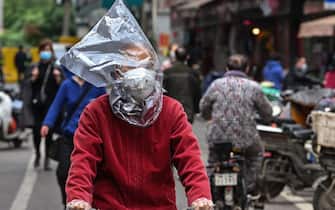 TOPSHOT - A man wearing a face mask and a plastic bag on his head rides a bicycle on a street in Wuhan, China's central Hubei province on April 14, 2020. - China has largely brought the coronavirus under control within its borders since the outbreak first emerged in the city of Wuhan late last year. (Photo by Hector RETAMAL / AFP) (Photo by HECTOR RETAMAL/AFP via Getty Images)
