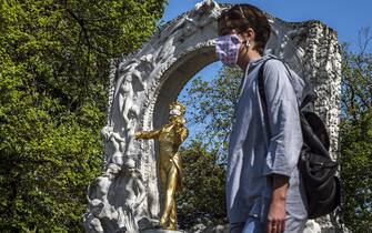 epa08379984 A woman wearing a protective face mask passes by the Johann Strauss Monument adorned with a protective face mask, during the ongoing pandemic of the COVID-19 disease caused by the SARS-CoV-2 coronavirus, at the Stadtpark (City Park) in Vienna, Austria, 23 April 2020.  EPA/CHRISTIAN BRUNA