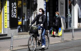 epa08393227 A woman wearing a protective face mask passes by fashion shops while another rides her bicycle in Central Zagreb, Croatia, 30 April 2020.  Croatia is easing the restrictive measures declared to prevent the spread of the SARS-CoV-2 coronavirus which causes the COVID-19 disease, by lifting the ban on public transport and reopening cultural institutions, sport centers, libraries and stores.  EPA/ANTONIO BAT