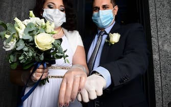 Newly-wed Italians Ester Concilio (L) and Rafaele Carbonelli wearing face masks show wedding rings under the protective gloves following the ceremony at the Briosco's town hall, about 45 km ( 28 miles) north of Milan, on May 11, 2020 during the country's lockdown aimed at curbing the spread of the COVID-19 infection, caused by the novel coronavirus. (Photo by Miguel MEDINA / AFP) (Photo by MIGUEL MEDINA/AFP via Getty Images)