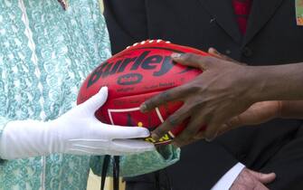Queen Elizabeth II accepts an Australian Rules football given to her during a visit to the Clontarf Aboriginal College in Perth.