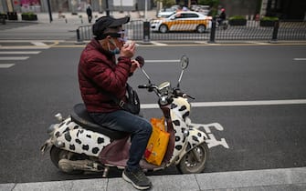 A man smokes a cigarette on his scooter in Wuhan, in China's central Hubei province on April 10, 2020. (Photo by Hector RETAMAL / AFP) (Photo by HECTOR RETAMAL/AFP via Getty Images)