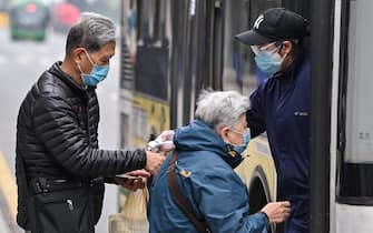 A bus employee wearing goggles and a face mask checks the temperature of passengers before they board a bus in Wuhan, in China's central Hubei province on April 10, 2020. (Photo by Hector RETAMAL / AFP) (Photo by HECTOR RETAMAL/AFP via Getty Images)
