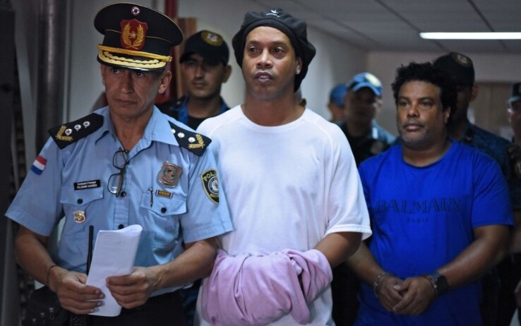Il fenomeno brasiliano, con le manette ai polsi nascoste da un panno rosa, condotto nel Palazzo di Giustizia di Asuncion, in Paraguay, per l'udienza che ne ha stabilito la cauzione