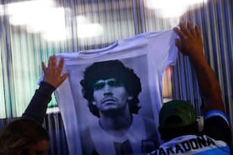 OLIVOS, ARGENTINA - NOVEMBER 03: Fans hold a jersey with the face of Diego Maradona at ClÃ­nica Olivos on November 03, 2020 in Olivos, Argentina. Personal doctor of Maradona, Leopoldo Luque, confirmed the former footballer will under a surgery to treat a clot in his brain. Maradona, who turned 60 on Friday 30, had spent the night of Monday hospitalized after being admitted with symptoms of depression. (Photo by Marcos Brindicci/Getty Images)
