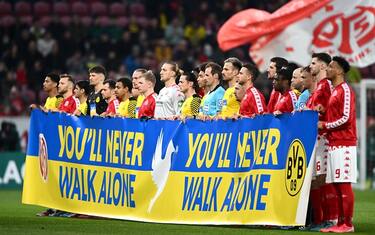 MAINZ, GERMANY - MARCH 16: Players from both teams and  match officials hold a banner with the Ukrainian flag to indicate peace and sympathy with Ukraine prior to the Bundesliga match between 1. FSV Mainz 05 and Borussia Dortmund at Opel Arena on March 16, 2022 in Mainz, Germany. (Photo by Alexander Scheuber/Getty Images)