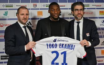 1195101856 Olympique Lyonnais's newly recruited Cameroonian forward Karl Toko Ekambi (C) poses with his jersey next to Head of Lyon's recruitment unit Florian Maurice (L) and Olympique Lyonnais Brazilian sports director Juninho (R), during a press conference on January 21, 2020, at the Groupama Stadium in Decines-Charpieu near Lyon, central-eastern France. (Photo by PHILIPPE DESMAZES / AFP) (Photo by PHILIPPE DESMAZES/AFP via Getty Images)