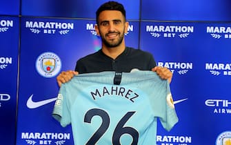 New Manchester City signing Riyad Mahrez holds up his shirt during the press conference at the City Football Academy, Manchester. (Photo by Richard Sellers/PA Images via Getty Images)