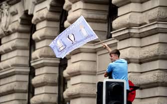 A Manchester City fans waves a flag after he climbed up a set of traffic lights, ahead of the Treble Parade in Manchester. Manchester City completed the treble (Champions League, Premier League and FA Cup) after a 1-0 victory over Inter Milan in Istanbul secured them Champions League glory. Picture date: Monday June 12, 2023.
