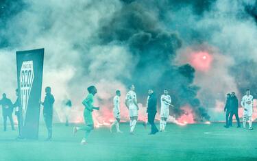 AS Saint-Etienne and SCO Angers football players react on the pitch after AS Saint-Etienne supporters launched smoke canisters to protest against the last place of their football club in the ranking of the French L1 championship, prior to the start of the French L1 football match between AS Saint-Etienne and SCO Angers at the Geoffroy Guichard stadium in Saint-Etienne, central France, on October 22, 2021. - Incidents broke out during the pre-match protocol Saint-Etienne/Angers of the 11th day of Ligue 1, caused by the ultras groups of the club stéphanois, and the kickoff of the game scheduled for 21:00 has been delayed. (Photo by PHILIPPE DESMAZES / AFP) (Photo by PHILIPPE DESMAZES/AFP via Getty Images)