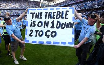 MANCHESTER, ENGLAND - MAY 21: Fans of Manchester City hold a sign which reads "The Treble Is On, 1 Down, 2 To Go" as they invade the pitch after the final whistle of the Premier League match between Manchester City and Chelsea FC at Etihad Stadium on May 21, 2023 in Manchester, England. (Photo by Michael Regan/Getty Images)