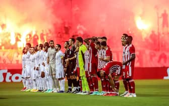 epa09357181 Players of Neftci (L) and Olympiacos (R) line up while supporters light flares prior to the UEFA Champions League second qualifying round, first leg soccer match between Olympiacos Piraeus and Neftci Baku in Piraeus, Greece, 21 July 2021.  EPA/PANAGIOTIS MOSCHANDREOU