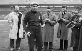 Benfica coach and manager Bela Guttmann (1900 - 1981) with a group of journalists at White City in London, 4th April 1962. He had just accused Tottenham Hotspur of watering the pitch at White Hart Lane, in preparation for their game against Benfica the next day. The match was the second leg semi-final of the European Cup.  (Photo by Keystone/Hulton Archive/Getty Images)