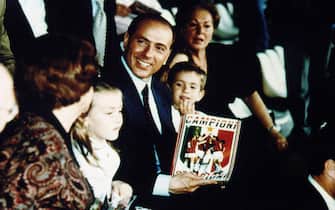 MILAN, ITALY - JANUARY 01:  Silvio Berlusconi, President of football team A.C. Milan, his mother Rosa Bossi (R) and his children Eleonora and Luigi hold a pennant celebrating the victory of the 12th championship of the Italian serie A won by his team as they attend a match at the Giuseppe Meazza San Siro Stadium in 1992 ca. in Milan, Italy.  (Photo by Franco Origlia/Getty Images)