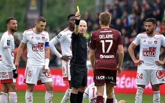Referee Florent Batta (C) gives a yellow card to Metzs French defender Thomas Delaine during the French L1 football match between FC Metz and Stade Brestois 29 (Brest) at Stade Saint-Symphorien in Longeville-les Metz, northern France on April 24, 2022. (Photo by Jean-Christophe Verhaegen / AFP) (Photo by JEAN-CHRISTOPHE VERHAEGEN/AFP via Getty Images)