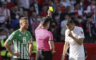 epa09789369 Referee Del Cerro (C) shows a yellow card to Sevilla's midfielder Joan Jordan (R) and Betis' midfielder Sergio Canales (L) during the Spanish LaLiga derby soccer match between Sevilla FC and Real Betis held at Ramon Sanchez Pizjuan stadium in Seville, southern Spain, 27 February 2022.  EPA/Jose Manuel Vidal