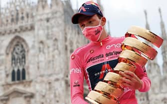 Overall race winner Team Ineos rider Great Britain's Tao Geoghegan Hart wearing the leader's pink jersey holds the "Never ending trophy" (Trofeo Senza Fine) as he celebrates on podium in front of the Duomo cathedral, after the the 21st and final stage of the Giro d'Italia 2020 cycling race, a 15,7-kilometer route between Cernusco sul Naviglio and Milano on October 25, 2020. (Photo by Luca Bettini / AFP)