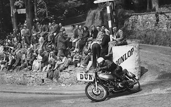 Spectators watch as Robert Leslie (Les) Graham DFC of Great Britain rides the #4 AJS Porcupine 500cc motorcycle around Governor's Bridge hairpin during the Isle of Man Senior TT Tourist Trophy motorcycle race on 18 June 1950 at Douglas, Isle of Man, United Kingdom. (Photo by Fox Photos/Hulton Archive/Getty Images).