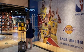 BEIJING, CHINA - OCTOBER 09: A Chinese woman stands next to a billboard showing players from the Los Angeles Lakers and advertising their upcoming exhibition game against the Brooklyn Nets in Shanghai, outside the NBA flagship retail store on October 9, 2019 in Beijing, China. The NBA is trying to salvage its brand in China amid criticism of its handling of a controversial tweet that infuriated the government and has jeopardized the leagues Chinese expansion. The crisis, triggered by a Houston Rockets executives tweet that praised protests in Hong Kong, prompted the Chinese Basketball Association to suspend its partnership with the league. The backlash continued with state-owned television CCTV scrapping its plans to broadcast pre-season games in Shanghai and Shenzhen, and the cancellation of other promotional fan events.  The league issued an apology, though NBA Commissioner Adam Silver angered Chinese officials further when he defended the right of players and team executives to free speech. China represents a lucrative market for the NBA, which stands to lose millions of dollars in revenue and threatens to alienate Chinese fans.  Many have taken to Chinas social media platforms to express their outrage and disappointment that the NBA would question the countrys sovereignty over Hong Kong which has been mired in anti-government protests since June.(Photo by Kevin Frayer/Getty Images)
