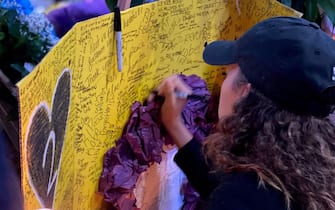 A woman writes words at a makeshift memorial for late basketball legend Kobe Bryant at the Staples center in Los Angeles on January 26, 2020, a few hours after the announcement of his death in a helicopter crash. - Nine people were killed in the helicopter crash which claimed the life of NBA star Kobe Bryant and his 13 year old daughter, Los Angeles officials confirmed on Sunday. Los Angeles County Sheriff Alex Villanueva said eight passengers and the pilot of the aircraft died in the accident. The helicopter crashed in foggy weather in the Los Angeles suburb of Calabasas. Authorities said firefighters received a call shortly at 9:47 am about the crash, which caused a brush fire on a hillside. (Photo by Chris Delmas / AFP) (Photo by CHRIS DELMAS/AFP via Getty Images)