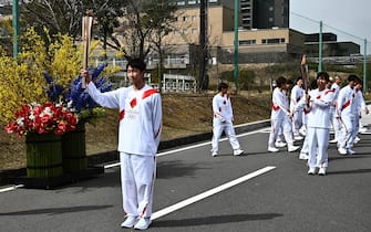 epa09095219 Japanese high school student Asato Owada poses with the Olympic Torch after receiving the flame from Azusa Iwashimizu, a member of Japan women's national football team, during the torch relay grand start outside J-Village National Training Centre in Naraha, Fukushima Prefecture, Japan, 25 March 2021. The postponed Tokyo 2020 Olympic Games are scheduled to start on 23 July 2021 and some 10,000 torchbearers will run across the country along a 121-day journey.  EPA/PHILIP FONG / POOL
