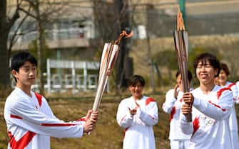 epa09095171 Japanese torchbearer Azusa Iwashimizu (R), a member of Japan women's national football team, passes the Olympic flame to the high school student Asato Owada at a torch kiss point during the torch relay grand start outside J-Village National Training Centre in Naraha, Fukushima Prefecture, Japan, 25 March 2021.  EPA/PHILIP FONG / POOL