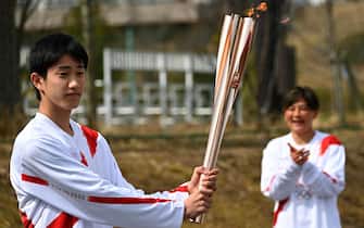 epa09095238 Japanese high school student Asato Owada (L) holds an Olympic Torch after receiving the flame during the torch relay grand start outside J-Village National Training Centre in Naraha, Fukushima Prefecture, Japan, 25 March 2021. The postponed Tokyo 2020 Olympic Games are scheduled to start on 23 July 2021 and some 10,000 torchbearers will run across the country along a 121-day journey.  EPA/PHILIP FONG / POOL