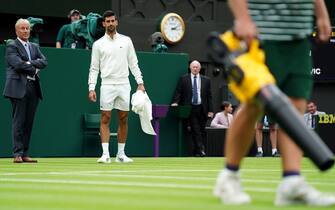 Novak Djokovic inspects the moisture on court and watches the ground staff who bring out leaf blowers to attempt to dry the grass during a rain delay in their match on day one of the 2023 Wimbledon Championships at the All England Lawn Tennis and Croquet Club in Wimbledon. Picture date: Monday July 3, 2023.