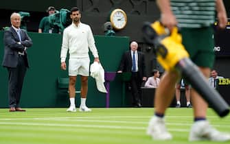 Novak Djokovic inspects the moisture on court and watches the ground staff who bring out leaf blowers to attempt to dry the grass during a rain delay in their match on day one of the 2023 Wimbledon Championships at the All England Lawn Tennis and Croquet Club in Wimbledon. Picture date: Monday July 3, 2023.