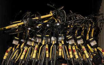 BEIJING, CHINA - MARCH 28: Chinese workers from the ride share bicycle company Ofo prepare to unload new bikes from a truck during rush hour on March 28, 2017 in Beijing, China. The popularity of bike shares has exploded in the past year with more than two dozen providers now battling for market share in major cities across China.  The bikes are hailed as an efficient, cheap, and environmentally-friendly solution for commuters, where riders unlock the stationless bicycles using a mobile phone app, drop them anywhere for the next user, and spend as little as 1 yuan ($0.15) per hour.  Given the bikes have several users a day — some of them inexperienced riders who swerve into traffic — they are often damaged, vandalized, or abandoned.  Companies like Ofo routinely collect the battered two-wheelers and bring them to a makeshift depot that is part repair shop, part graveyard where they are either salvaged or scrapped.  The bike shares are powering a cycling revival of sorts in a country once known as the “Kingdom of Bicycles”.  In the early years of Communist China, most Chinese aspired to own a bicycle as a marker of achievement.  When the country’s economic transformation made cars a more valued status symbol, the bicycle — a Chinese cultural icon — was mocked as a sign of backwardness.  The bike share craze is also a boon for manufacturers who are now mass producing over a million bikes a month to meet demand, and the number of shared bike users will reach 50 million in China by the end of the year, according to Beijing-based BigData Research.  Not everyone is cheering the revival though, as municipal officials are drafting new regulations to control the chaotic flood of bicycles on streets and sidewalks.   (Photo by Kevin Frayer/Getty Images)