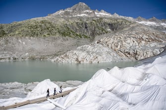 epa08553196 People visit the Rhone Glacier covered in blankets above Gletsch near the Furkapass in Switzerland, 18 July 2020. The Alps oldest glacier is protected by special white blankets to prevent it from melting.  EPA/URS FLUEELER