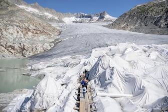 epa08553173 People visit the Rhone Glacier covered in blankets above Gletsch near the Furkapass in Switzerland, 18 July 2020. The Alps oldest glacier is protected by special white blankets to prevent it from melting.  EPA/URS FLUEELER