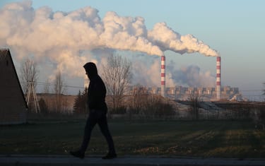 ROGOWIEC, POLAND - NOVEMBER 29: A man walks through the village of Kleszczow as steam and smoke rise from the Belchatow Power Station behind on November 29, 2018 at Rogowiec, Poland. The Belchatow station, with an output of 5,472 megawatts, is the world's largest lignite coal-fired power station. The station emits approximately 30 million tonnes of CO2 per year. The United Nations COP 24 climate conference is due to begin on December 2 in nearby Katowice, two hours south of Belchatow.  (Photo by Sean Gallup/Getty Images)