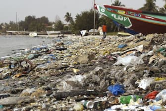 A picture taken on June 2, 2018, shows people walking on a beach covered with trash, including many plastic items, in the Hann Bay in Dakar. - World Environment  Day is marked annually on June 5, and aims at promoting awareness and action to protect the environment. Each World Environment Day is focused on a theme that spotlights a pressing environmental concern, with the theme for 2018 being Beat Plastic Pollution". (Photo by SEYLLOU / AFP)        (Photo credit should read SEYLLOU/AFP via Getty Images)