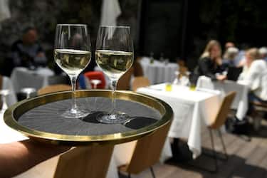 A waiter carries a tray with glasses of wine towards customers as they sit on a terrace of a restaurant in Marseille, southern France, on May 19, 2021, as cafes, restaurants and other businesses re-opened across France after closures during the coronavirus (Covid-19) pandemic. - Patrons have made their way back to cafes and prepared long-awaited visits to cinemas and museums as France loosened restrictions in a return to semi-normality after over six months of Covid-19 curbs. Cafes and restaurants with terraces or rooftop gardens can now offer outdoor dining, under the second phase of a lockdown-lifting plan that should culminate in a full reopening of the economy on June 30. (Photo by Nicolas TUCAT / AFP) (Photo by NICOLAS TUCAT/AFP via Getty Images)