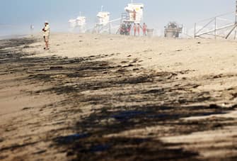 HUNTINGTON BEACH, CALIFORNIA - OCTOBER 03: A person stands near oil washed up on Huntington State Beach after a 126,000-gallon oil spill from an offshore oil platform on October 3, 2021 in Huntington Beach, California. The spill forced the closure of the popular Great Pacific Airshow with authorities urging people to avoid beaches in the vicinity.  (Photo by Mario Tama/Getty Images)