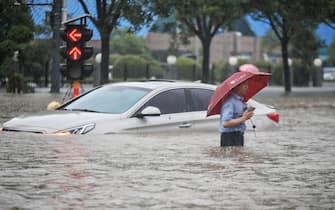 TOPSHOT - This photo taken on July 20, 2021 shows a man wading past a submerged car along a flooded street following heavy rains in Zhengzhou in China's central Henan province. - - China OUT (Photo by STR / AFP) / China OUT (Photo by STR/AFP via Getty Images)