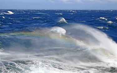 Rough seas of the southern pacific ocean, huge waves with rainbow showing in the foam coming from the top of the crashing waves, New Zealand
