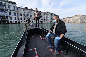 A gondolier (Rear) wearing a face mask resumes service on a Venice canal on May 18, 2020 during the country's lockdown aimed at curbing the spread of the COVID-19 infection, caused by the novel coronavirus. - Restaurants and churches reopen in Italy on May 18, 2020 as part of a fresh wave of lockdown easing in Europe and the country's latest step in a cautious, gradual return to normality, allowing businesses and churches to reopen after a two-month lockdown. (Photo by ANDREA PATTARO / AFP) (Photo by ANDREA PATTARO/AFP via Getty Images)