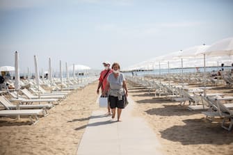 Due bagnanti camminano su una passerella di un lido attrezzato sulla spiaggia di Rimini