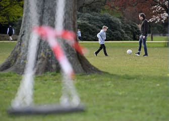 HAMBURG, GERMANY - APRIL 04: Boys play football behind a swing that is no longer allowed to be used next the Aussenalster during the coronavirus crisis on April 4 in Hamburg, Germany. The coronavirus and the disease it causes, Covid-19, are having a fundamental impact on society, government and the economy in Germany. Public life has been restricted to the essentials in an effort by authorities to slow the spread of infections. Hospitals are scrambling to increase their testing and care capacity. An economic recession seems likely as economic activity is slowed and many businesses are temporarily closed. Schools, daycare centers and universities remain shuttered. And government, both federal and state, seek to mobilize resources and find adequate policies to confront the virus and mitigate its impact. (Photo by Stuart Franklin/Getty Images)