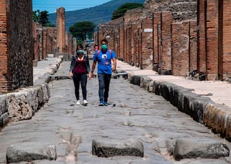 Visitors wearing a face mask walk across the archeological site of Pompeii on May 26, 2020, as the country eases its lockdown aimed at curbing the spread of the COVID-19 infection, caused by the novel coronavirus. - Italy's world-famous archeological site Pompeii reopened to the public on May 26,bBut with foreign tourists still prohibited from travel to Italy until June, the site that attracted just under 4 million visitors in 2019 is hoping that for now, Italian tourists can make up at least a fraction of the difference. (Photo by Tiziana FABI / AFP) (Photo by TIZIANA FABI/AFP via Getty Images)
